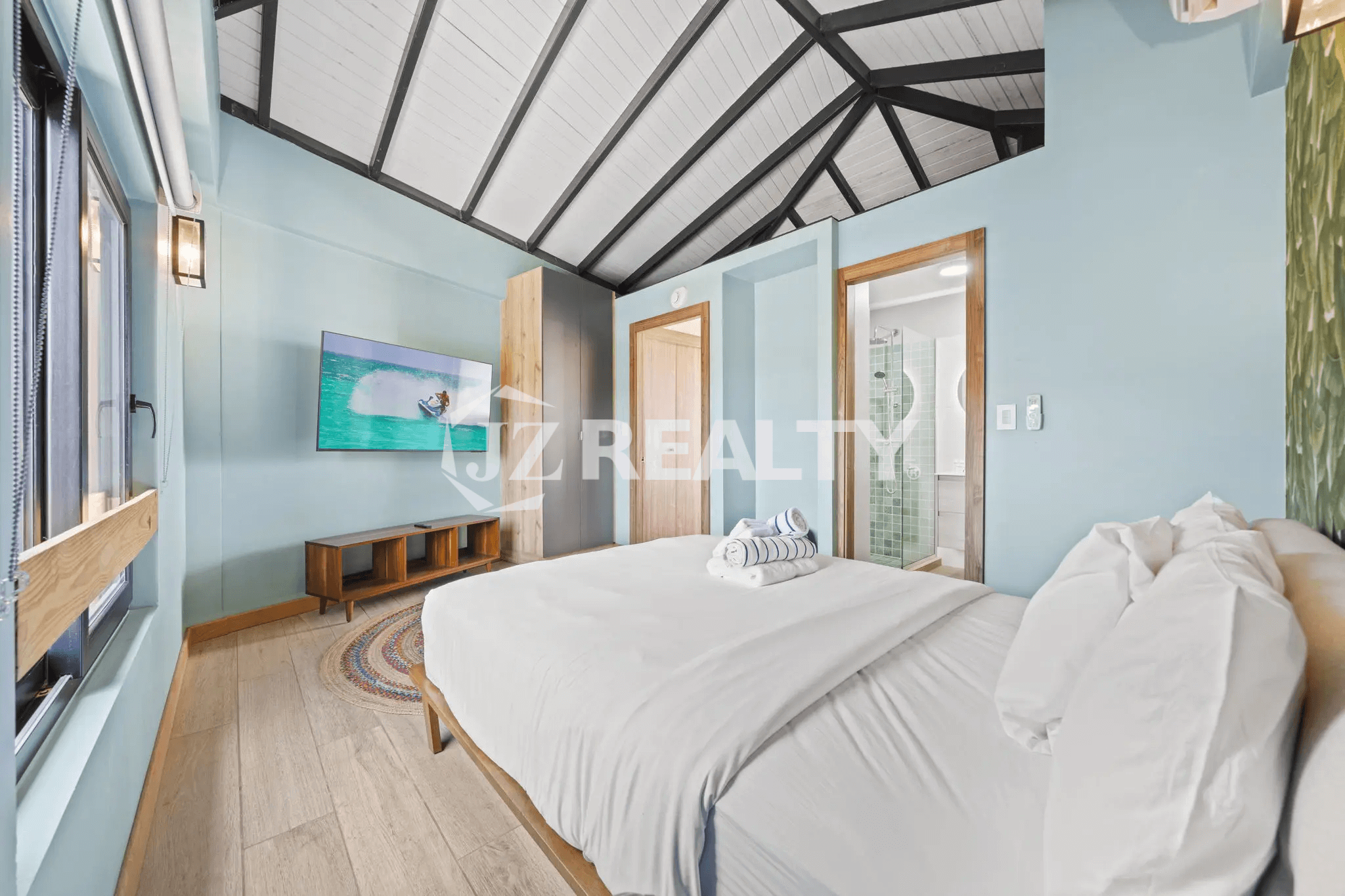 Bright bedroom in Porta al Sole Unit 13 with light blue walls, a dramatic vaulted white and black ceiling, king bed, and TV.