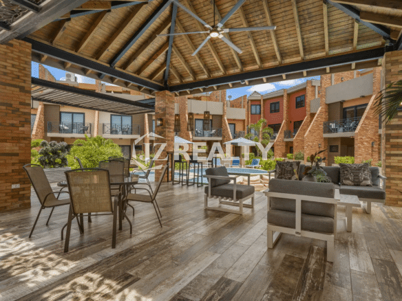 View of the spacious covered outdoor common area with a high wooden ceiling, ceiling fan, brick columns, and a mix of dining and casual seating areas overlooking the inner courtyard.