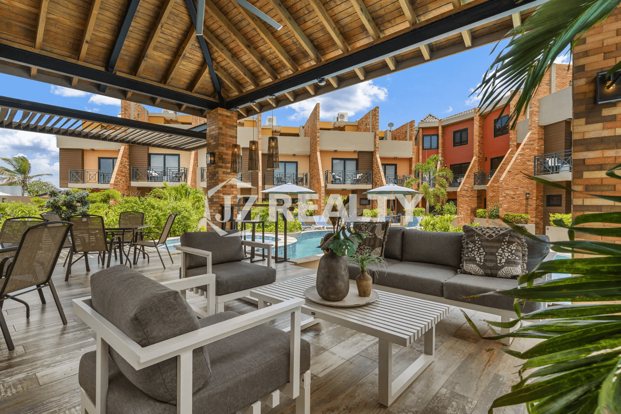 Detailed close-up of the luxurious covered patio/lounge area with contemporary gray and white outdoor furniture, including a sofa, armchairs, and coffee table, set under a large wooden roof.