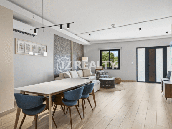 Open concept dining and living area in Porta al Sole Unit 13 with long white dining table, blue chairs, white sofa, and light wood floors.