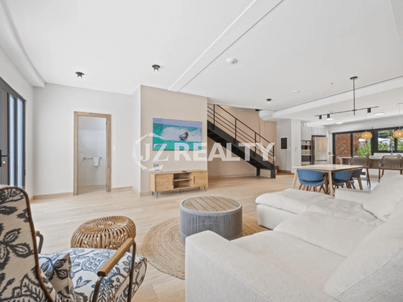 Spacious, open living room on the ground floor of Porta al Sole Unit 13 showing a sectional sofa, decorative chairs, and a black staircase leading up.