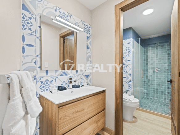 Guest bathroom in Porta al Sole Unit 13 featuring a wood vanity, white sink, decorative blue and white patterned tile backsplash, and a separate shower with teal tiles.