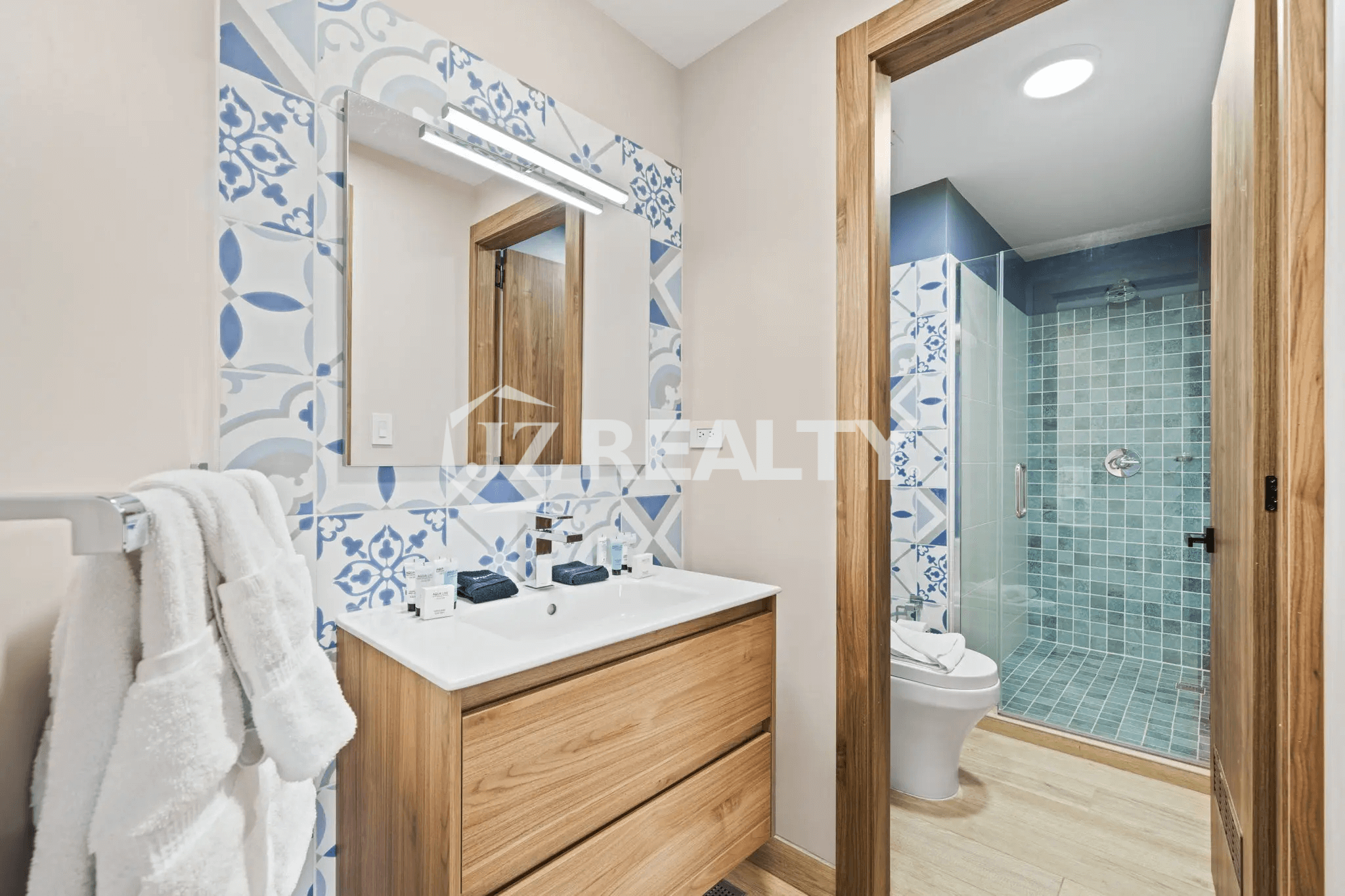 Guest bathroom in Porta al Sole Unit 13 featuring a wood vanity, white sink, decorative blue and white patterned tile backsplash, and a separate shower with teal tiles.