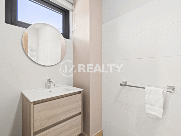 Small half bathroom or powder room in Porta al Sole Unit 13 with a wood vanity, white sink, circular mirror, and white wall tiles.
