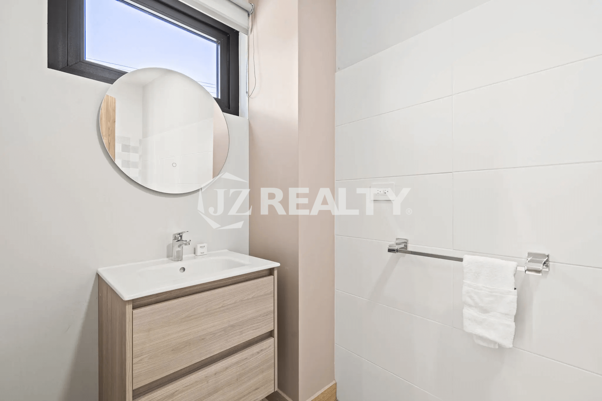 Small half bathroom or powder room in Porta al Sole Unit 13 with a wood vanity, white sink, circular mirror, and white wall tiles.