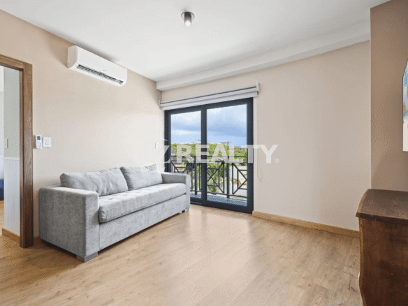 Interior view of a living room in Porta al Sole Unit 13 featuring a grey sofa, hardwood floor, AC unit, and glass door leading to a balcony.