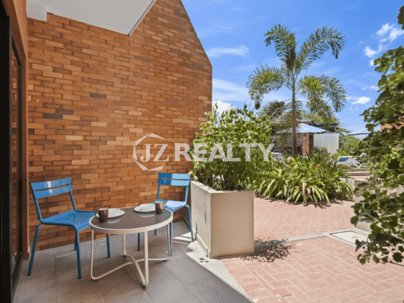 Private outdoor covered patio at Porta al Sole Unit 13 with a small table, two blue chairs, and a brick wall.