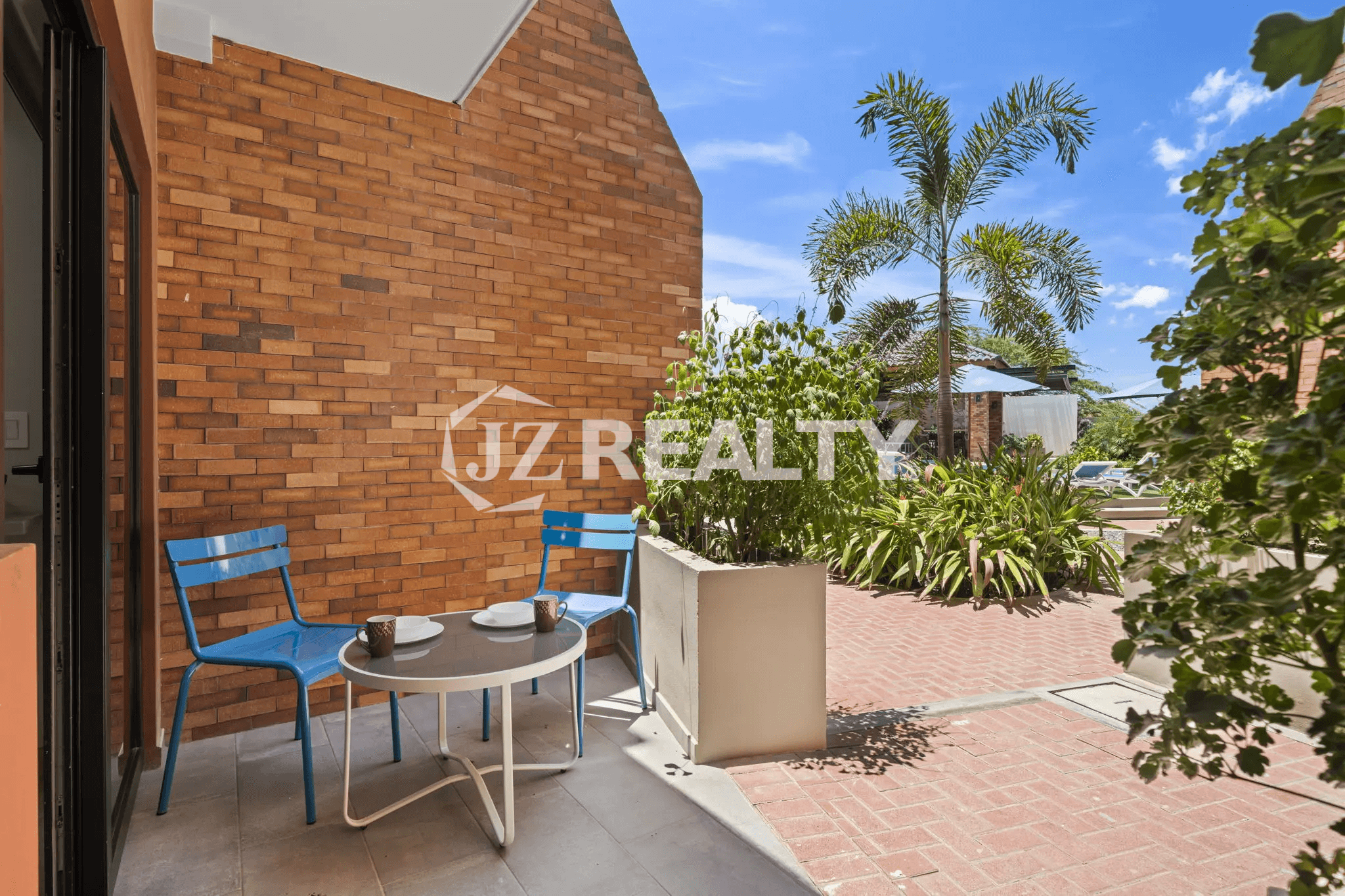 Private outdoor covered patio at Porta al Sole Unit 13 with a small table, two blue chairs, and a brick wall.