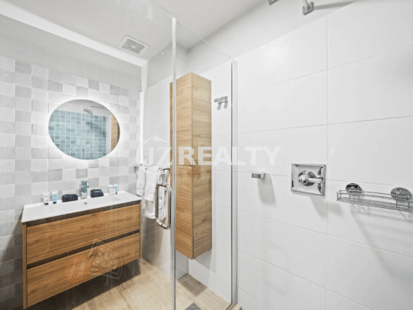 Stylish second bathroom in Porta al Sole Unit 13 with white wall tiles, wood-look vanity, mirror, and glass shower.