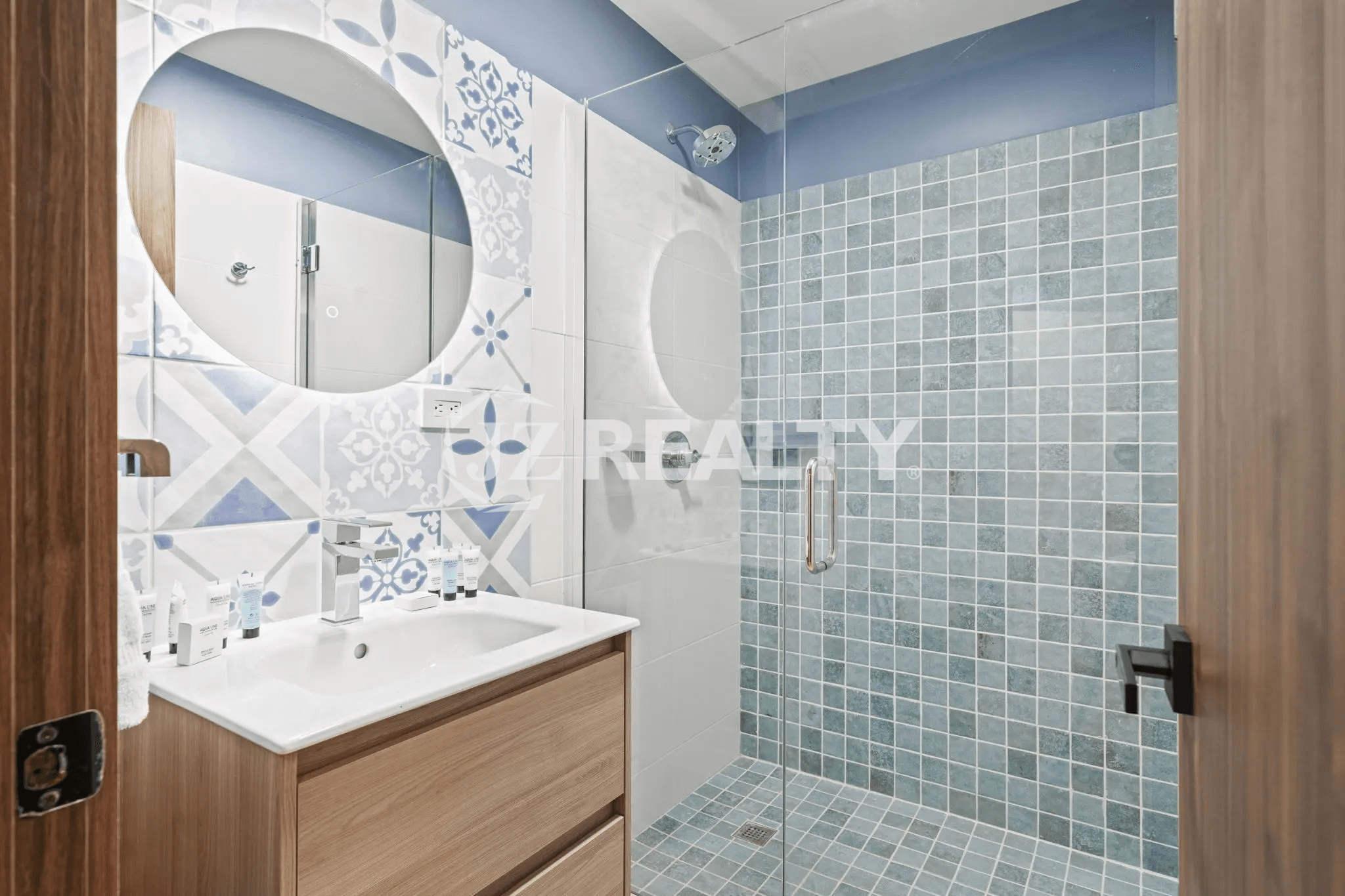 Second modern bathroom with wood vanity, round mirror, and walk-in shower with blue square and circular accent tiles in Porta al Sole Unit 14.