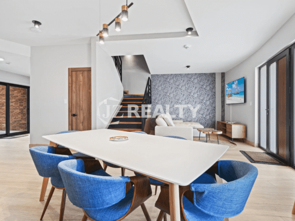 Open-concept living and dining area featuring a white table, blue dining chairs, and staircase in Porta al Sole Unit 14.