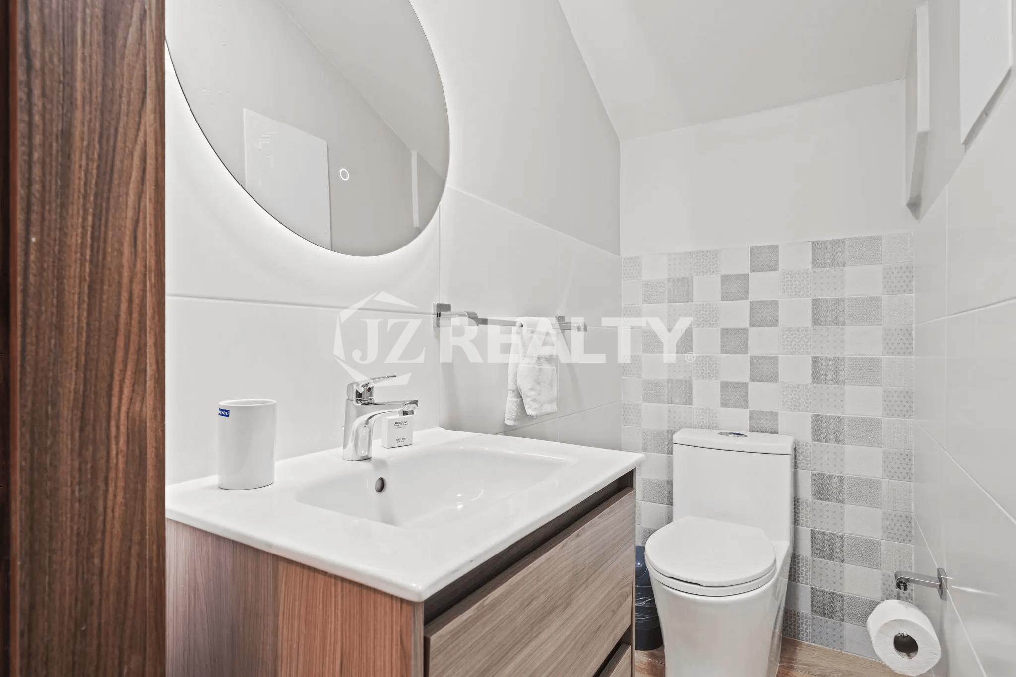 Modern powder room with a wood vanity, lighted circular mirror, and checkered accent tile wall in Porta al Sole Unit 14.