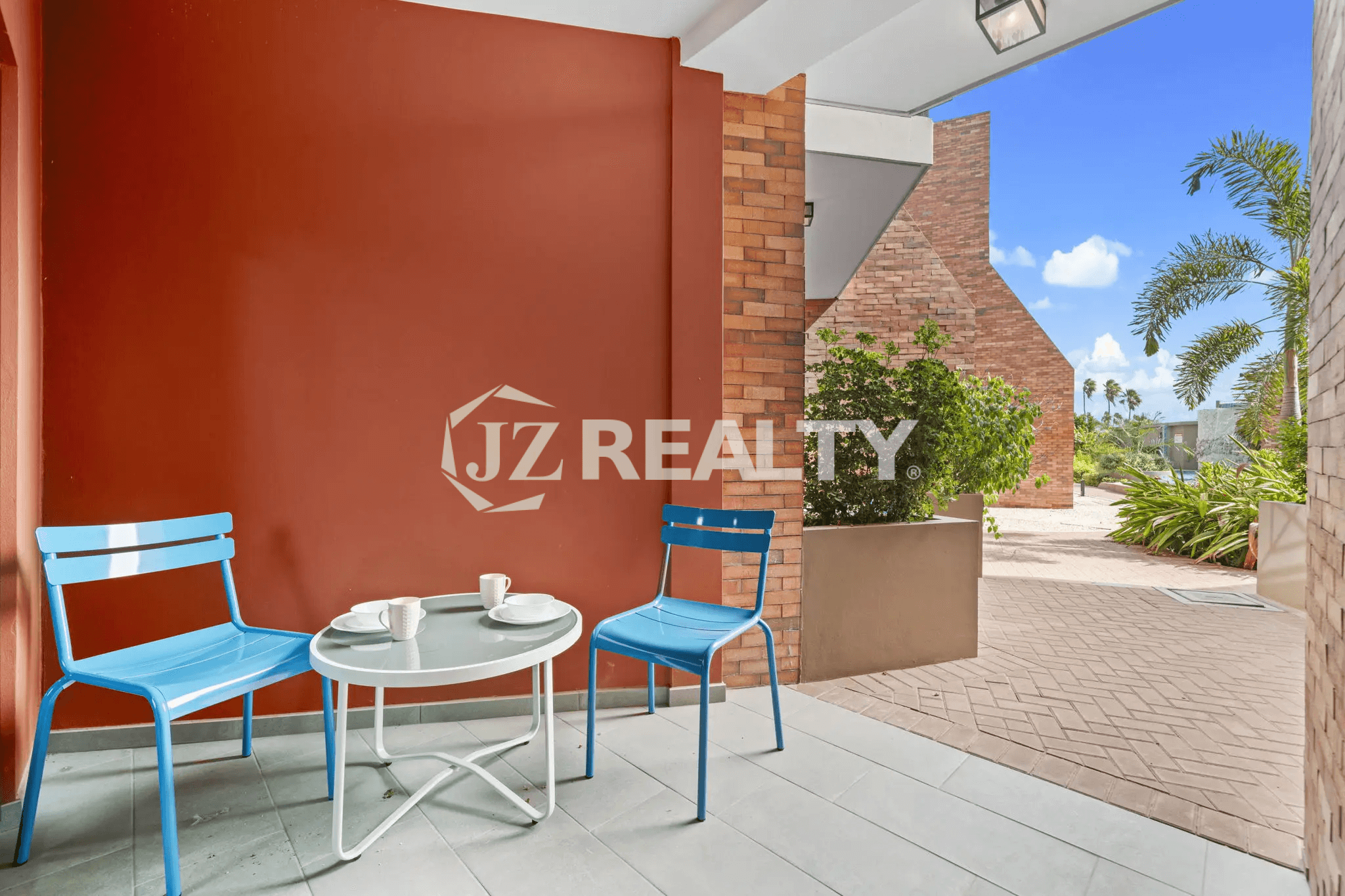 Small outdoor patio with an accent brick wall and blue metal chairs with a small table in Porta al Sole Unit 14.