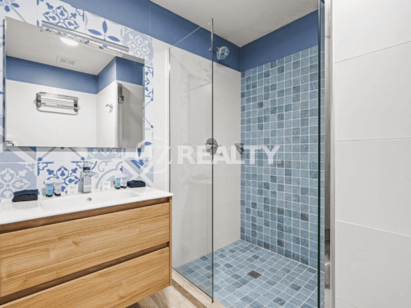 Modern bathroom featuring a glass-enclosed shower with blue and white mosaic tile, a wood vanity with a vessel sink, and a large wall mirror in Porta al Sole Unit 15.