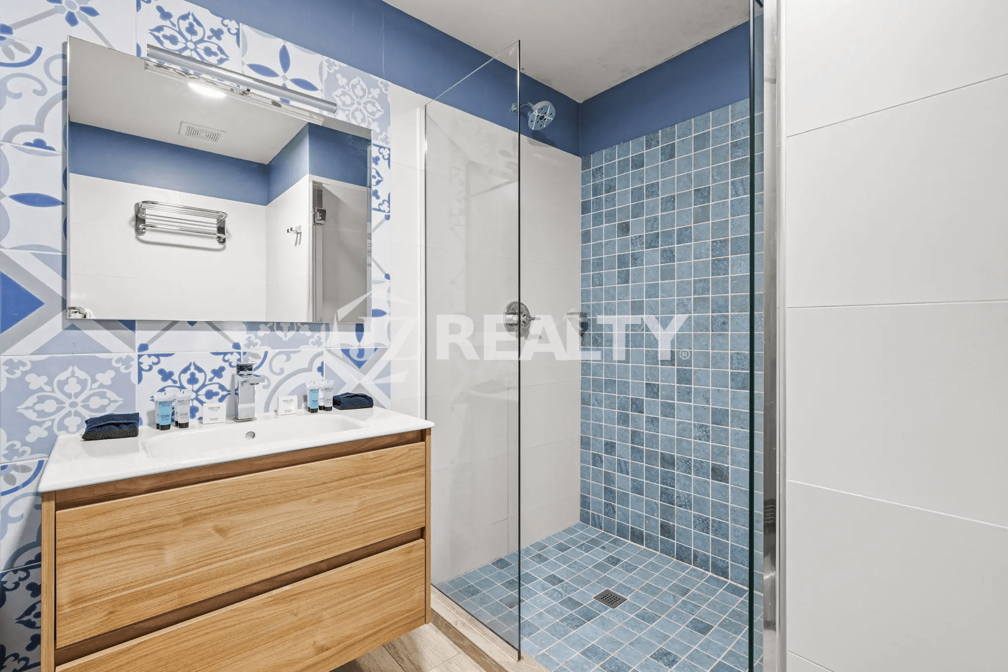 Modern bathroom featuring a glass-enclosed shower with blue and white mosaic tile, a wood vanity with a vessel sink, and a large wall mirror in Porta al Sole Unit 15.