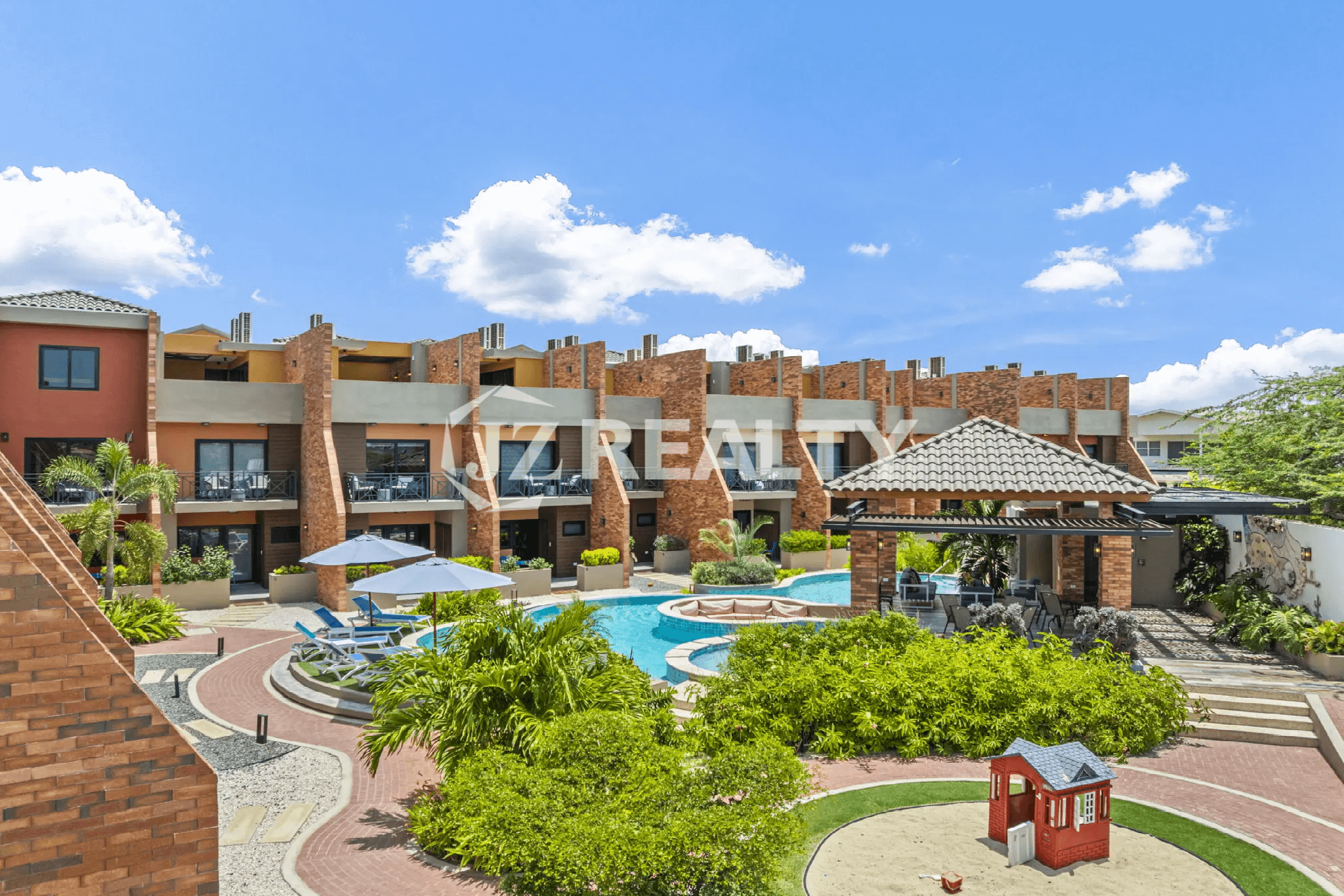 Aerial view of the Porta al Sole community pool and sun deck, showing the central gazebo, surrounding tropical landscaping, and the exterior of the multi-story residential buildings.