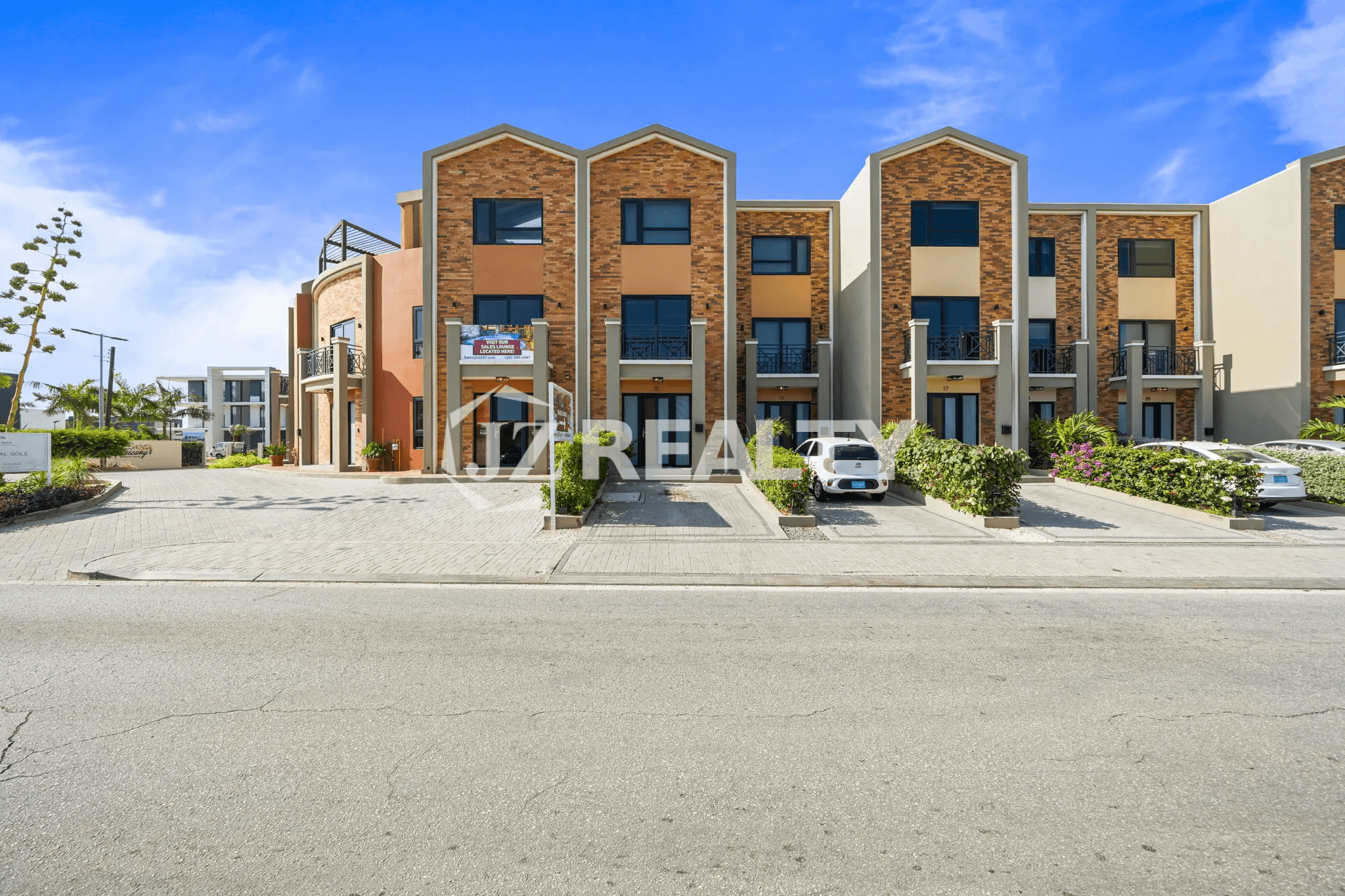 Exterior street view of the modern, multi-story Porta al Sole complex with red brick accents and landscaping, showing the building entrance and front parking area.
