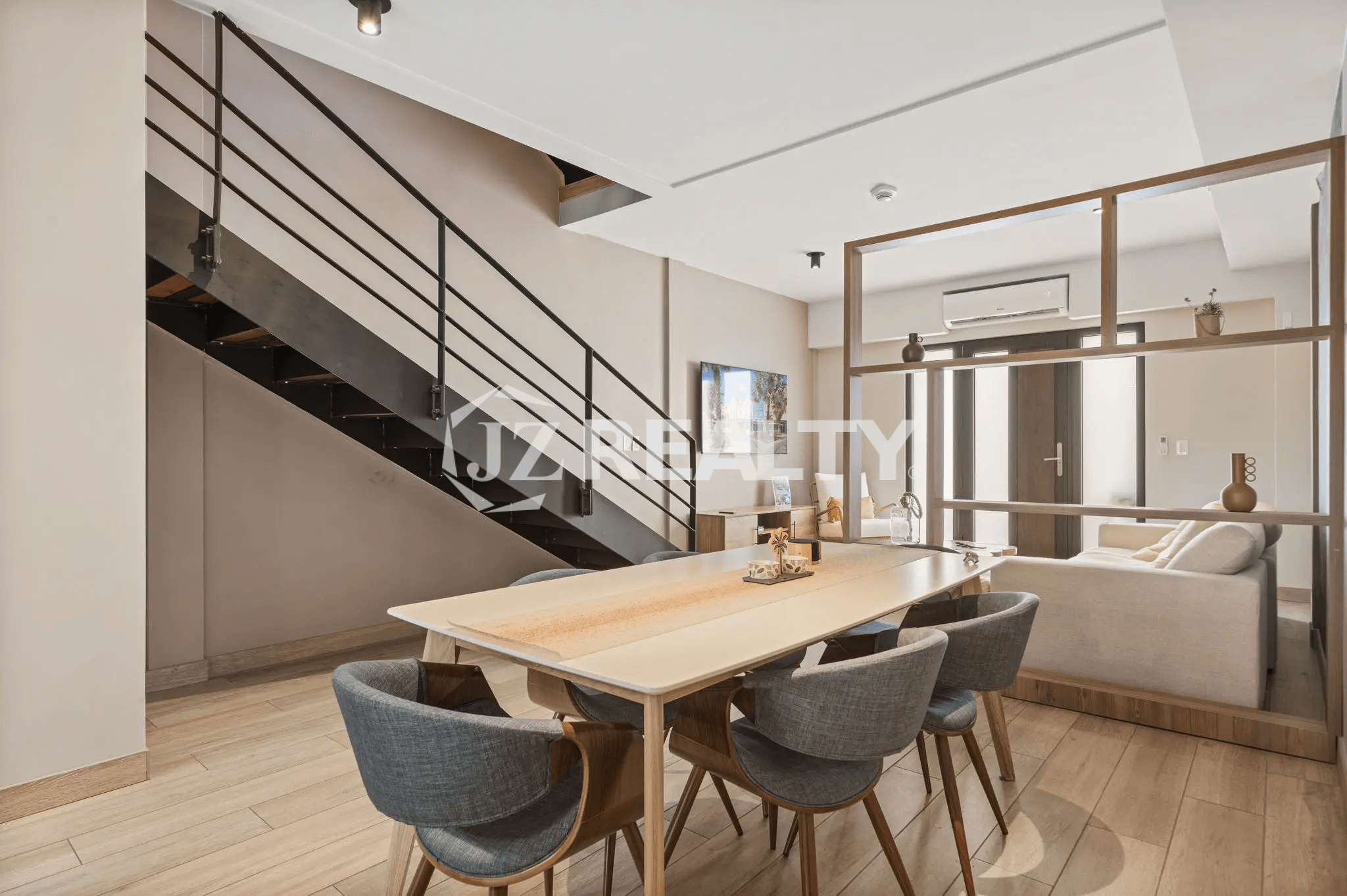 Dedicated dining area with a long light-wood table and gray upholstered chairs, located beneath the staircase, looking toward the living room in Porta al Sole Unit 15.