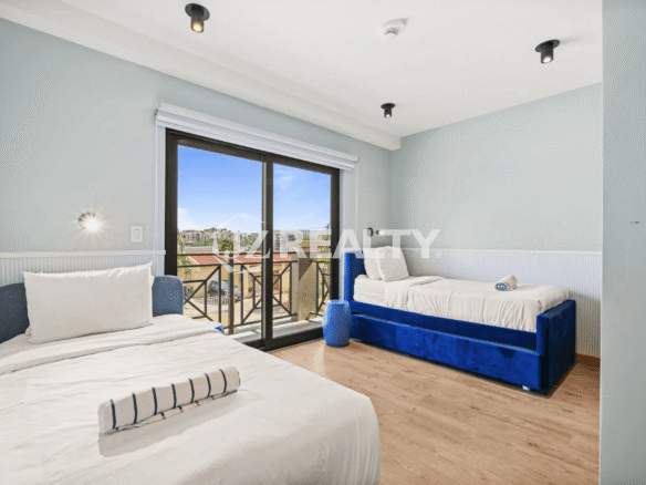 Guest bedroom with light blue walls, two twin beds with blue velvet frames, and a large sliding glass door leading to a private balcony in Porta al Sole Unit 15.