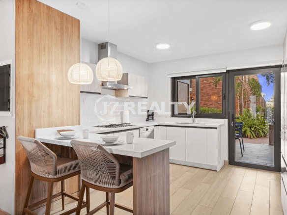 Modern kitchen featuring white cabinetry, subway tile backsplash, gas range, and a breakfast bar with woven rattan stools and pendant lighting, opening to the private patio in Porta al Sole Unit 15.