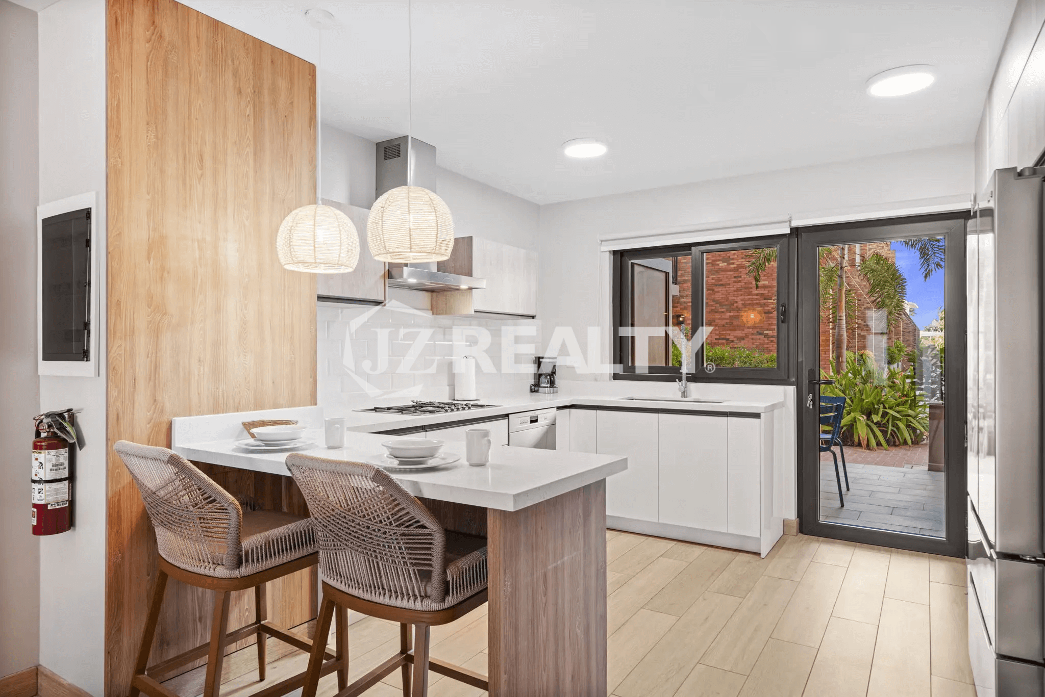 Modern kitchen featuring white cabinetry, subway tile backsplash, gas range, and a breakfast bar with woven rattan stools and pendant lighting, opening to the private patio in Porta al Sole Unit 15.
