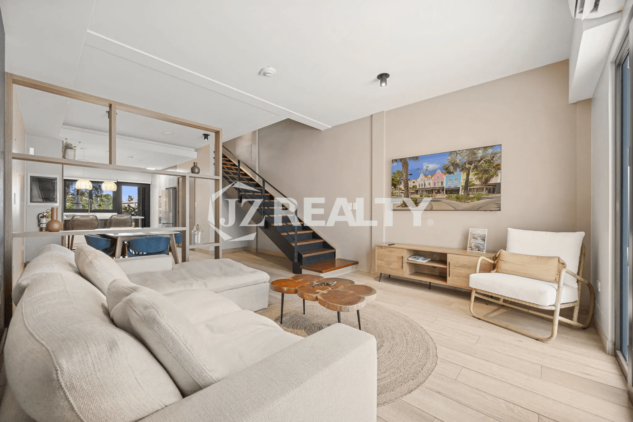 Wide-angle view of the bright, modern living room with a large TV, light wood media console, comfortable seating, and the sleek metal and wood open staircase in Porta al Sole Unit 15.