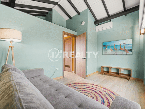 Bright, loft-style living room with sloped ceilings, a comfortable gray sofa, flat-screen TV, and decorative floor lamp in Porta al Sole Unit 15.