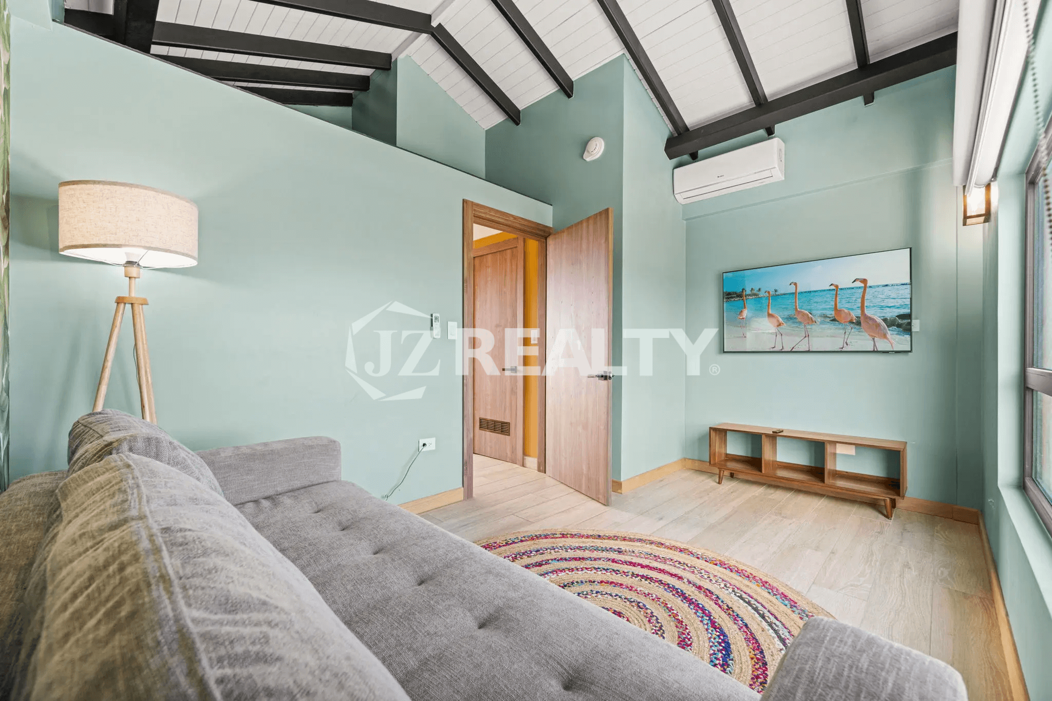 Bright, loft-style living room with sloped ceilings, a comfortable gray sofa, flat-screen TV, and decorative floor lamp in Porta al Sole Unit 15.