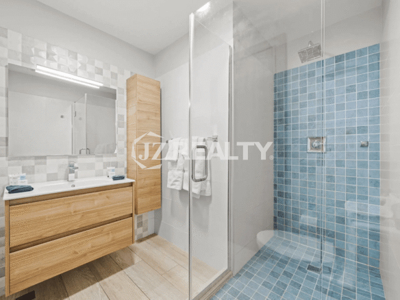 Spacious primary bathroom with a walk-in glass shower, large blue tile floor and accent wall, wood vanity, and a separate wooden storage cabinet in Porta al Sole Unit 15.