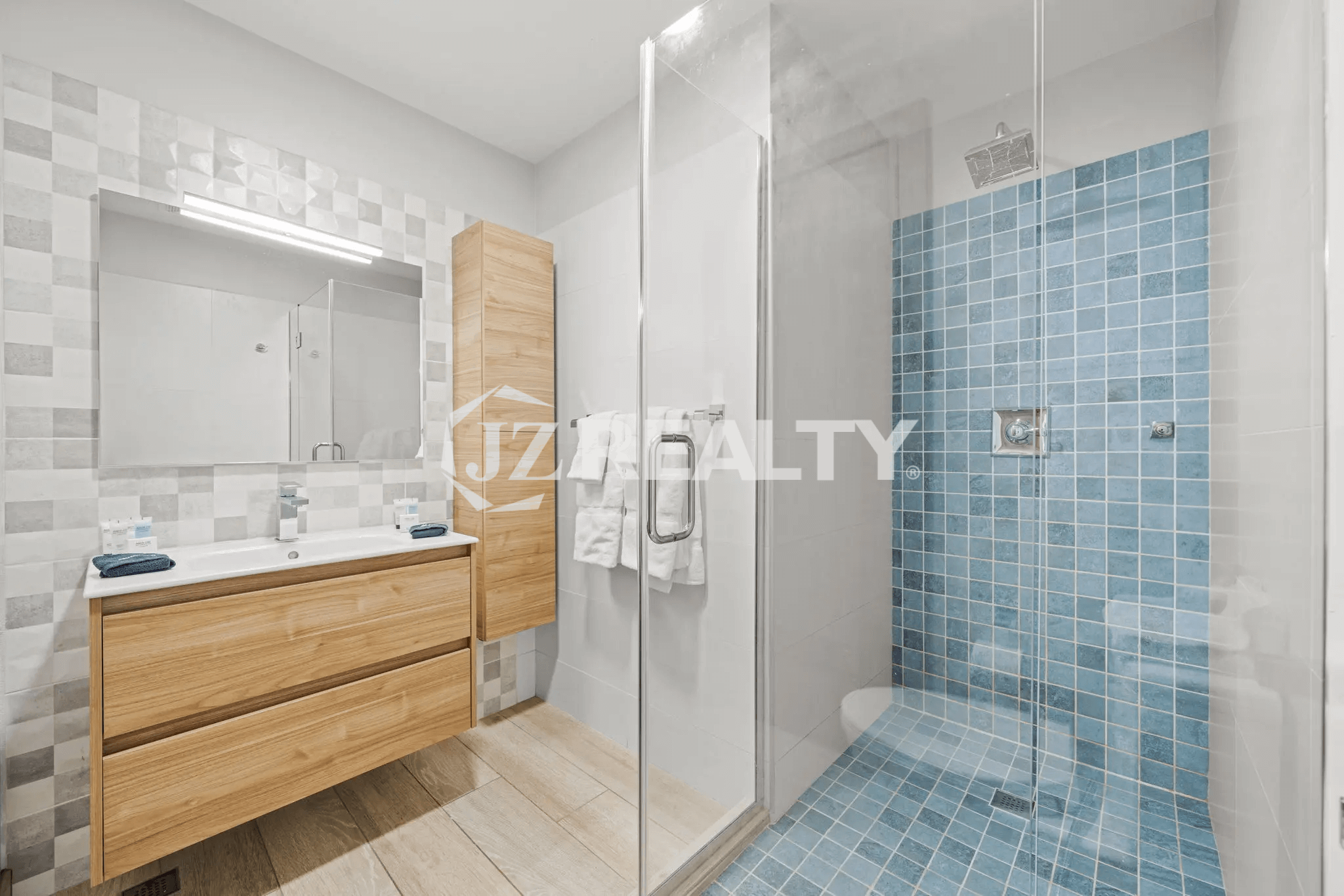 Spacious primary bathroom with a walk-in glass shower, large blue tile floor and accent wall, wood vanity, and a separate wooden storage cabinet in Porta al Sole Unit 15.