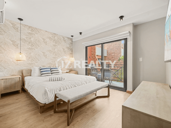 Primary bedroom featuring a queen-size bed, a tropical leaf-patterned accent wall, stylish pendant lighting, and a sliding glass door to a private balcony in Porta al Sole Unit 15.