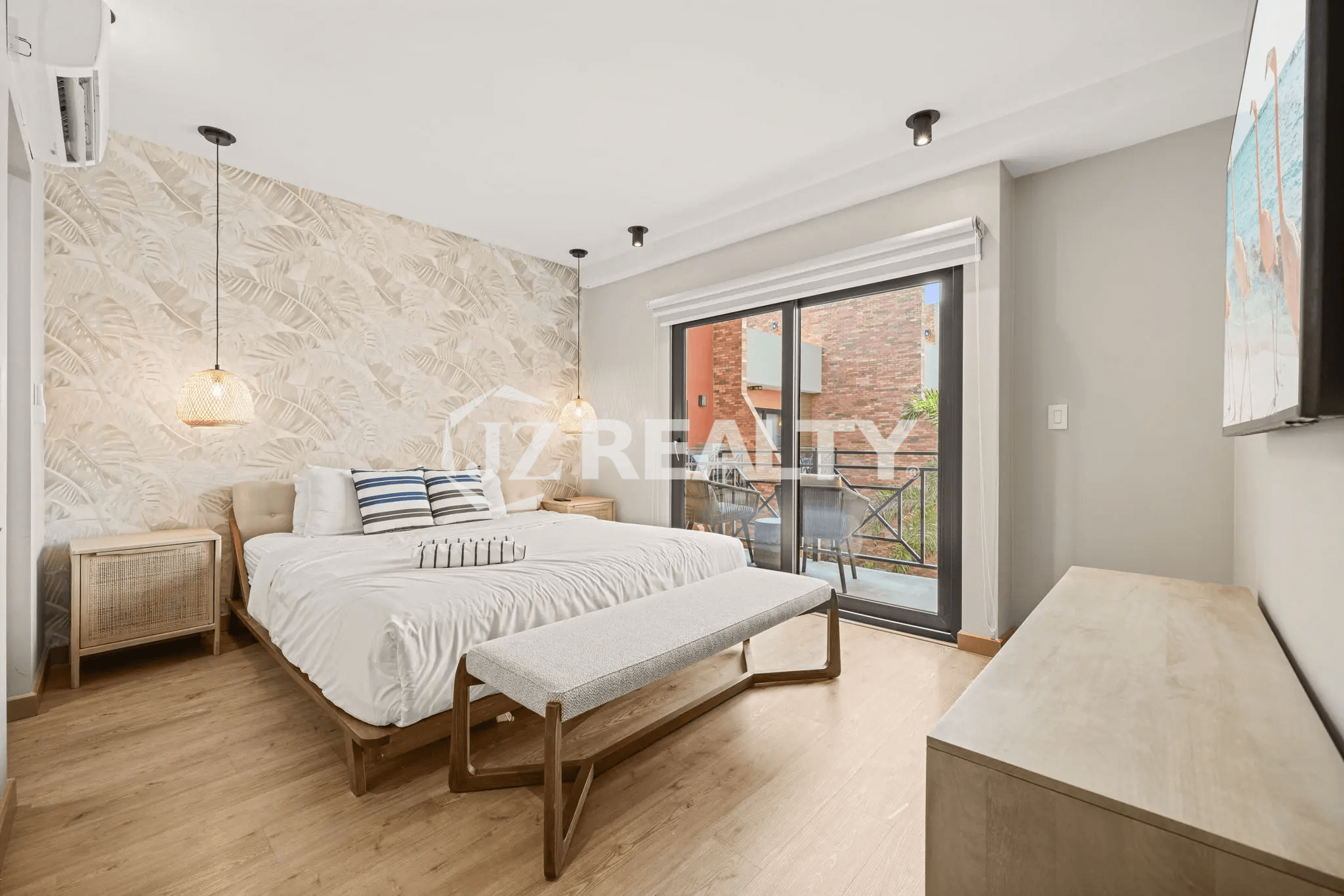 Primary bedroom featuring a queen-size bed, a tropical leaf-patterned accent wall, stylish pendant lighting, and a sliding glass door to a private balcony in Porta al Sole Unit 15.