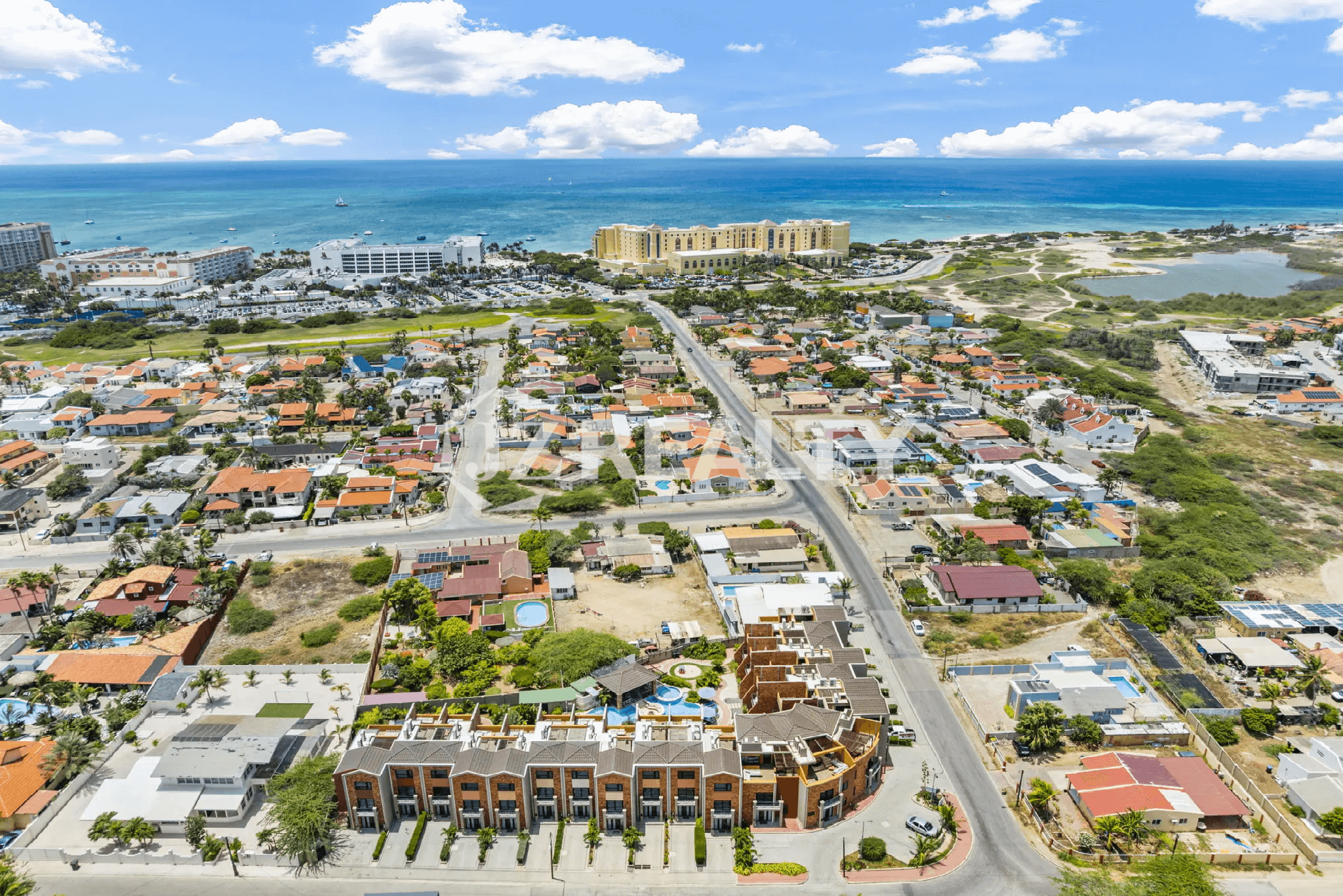 Wide aerial view of the Porta al Sole community in the foreground, with the surrounding residential area, main road, and the coastal hotel area leading to the Caribbean Sea in the background.