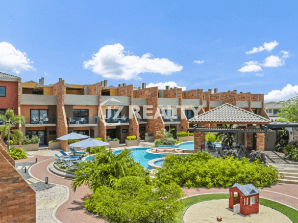 Elevated view of the Porta al Sole community, showcasing the central swimming pool, landscaped grounds, lounge chairs, a small children's play area, and the surrounding townhouse buildings.