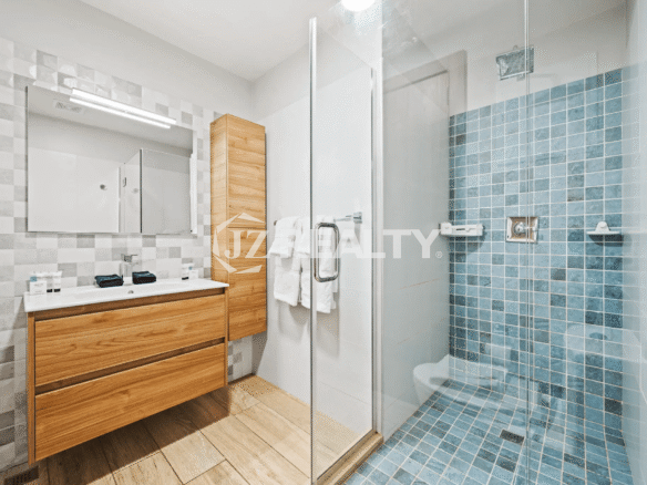 Full bathroom with a long wood vanity, mirrored medicine cabinet, a separate wood storage cabinet, and a walk-in shower with blue mosaic tiles.