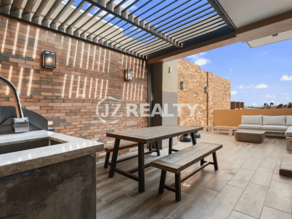 Large rooftop terrace featuring a wood-slat pergola, an outdoor dining table with benches, a built-in BBQ/sink area, and an outdoor sectional sofa.