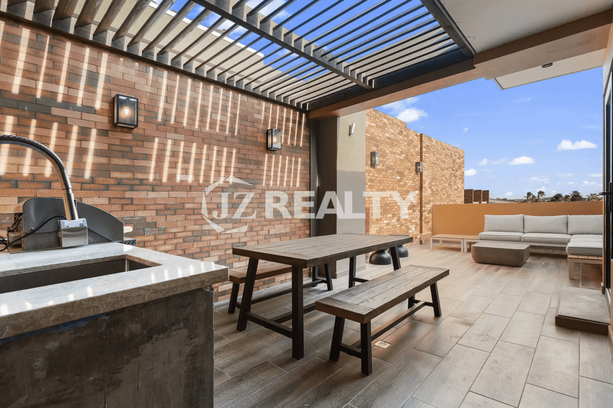 Large rooftop terrace featuring a wood-slat pergola, an outdoor dining table with benches, a built-in BBQ/sink area, and an outdoor sectional sofa.