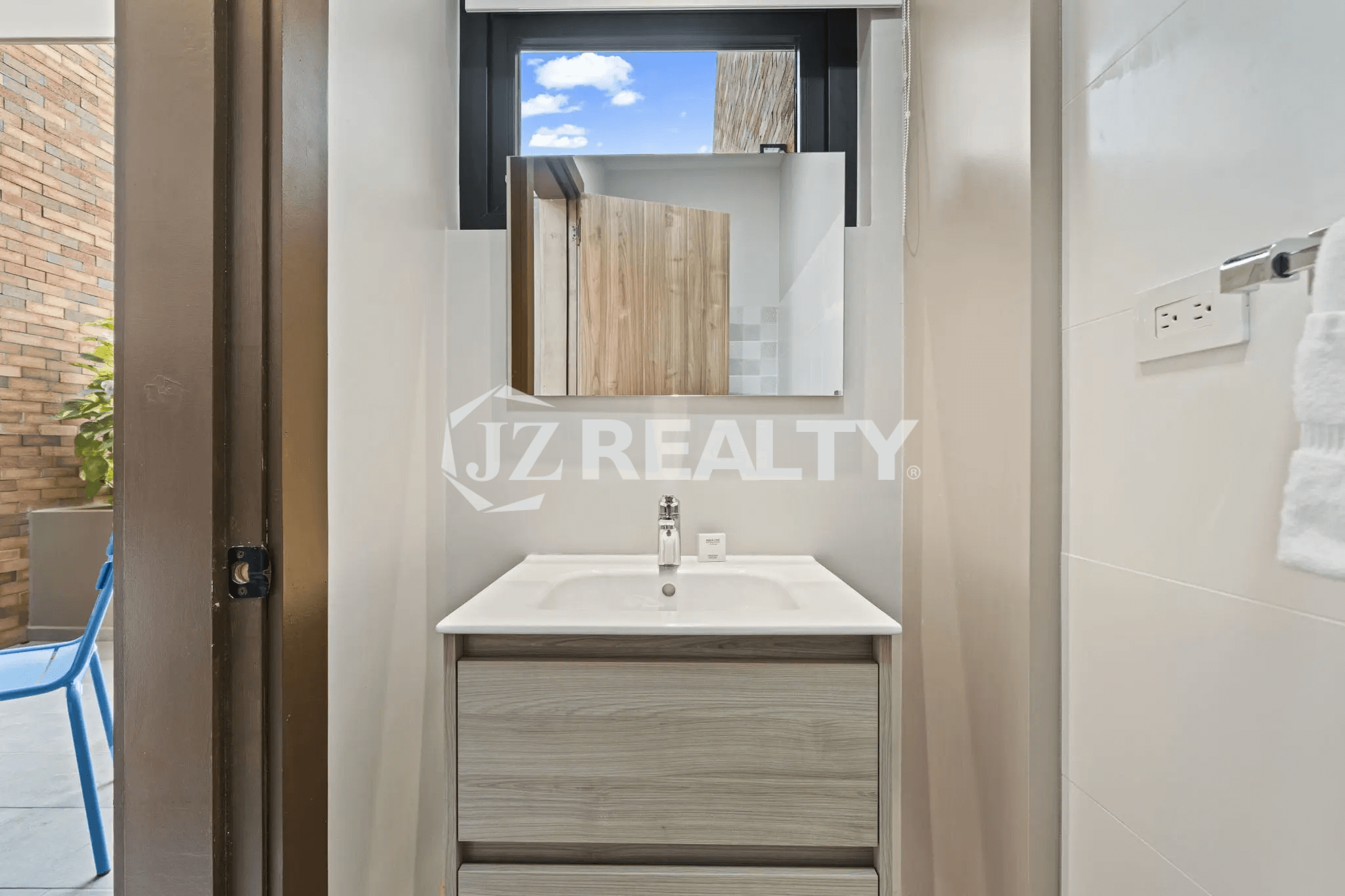 Close-up of a small bathroom sink area with a gray vanity, rectangular mirror, white sink, and white wall tiles.