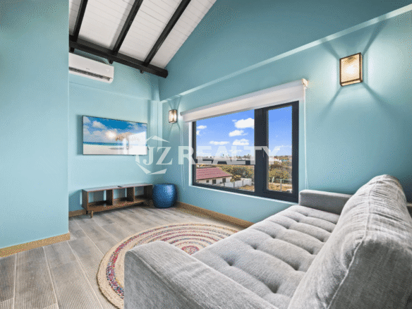 Cozy upstairs seating area with sky blue walls, vaulted ceiling, a gray tufted sofa, a window with a view, and a wall-mounted TV.