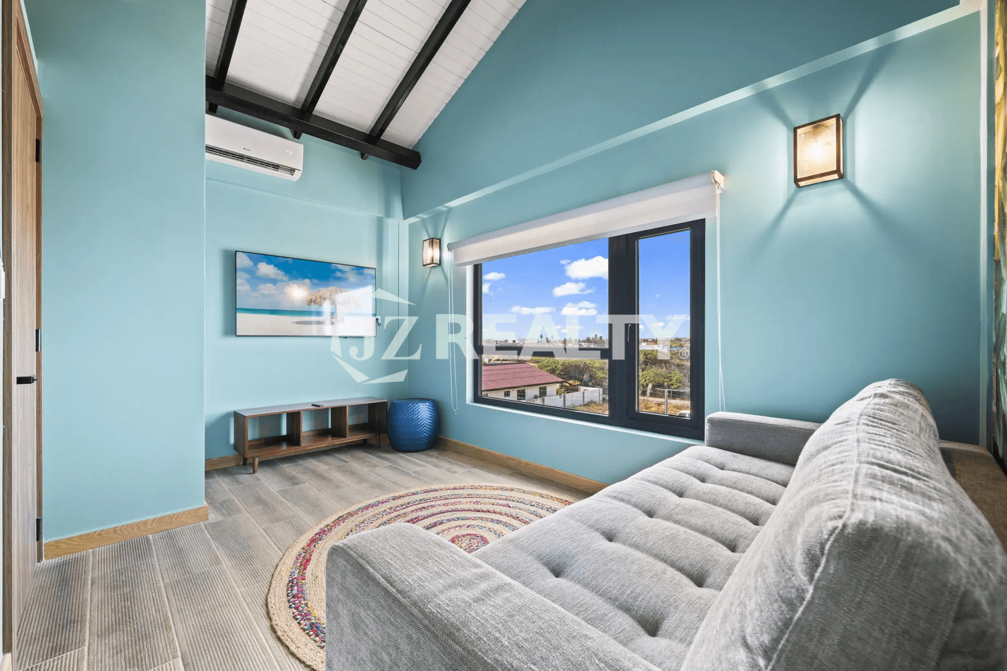 Cozy upstairs seating area with sky blue walls, vaulted ceiling, a gray tufted sofa, a window with a view, and a wall-mounted TV.