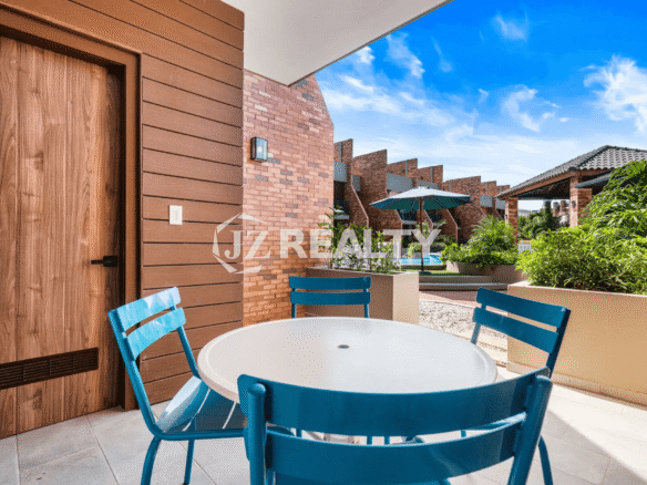 Covered outdoor patio space at Porta al Sole Unit 18 with a small round white table and three blue chairs, showing the view to the resort's exterior and pool area.