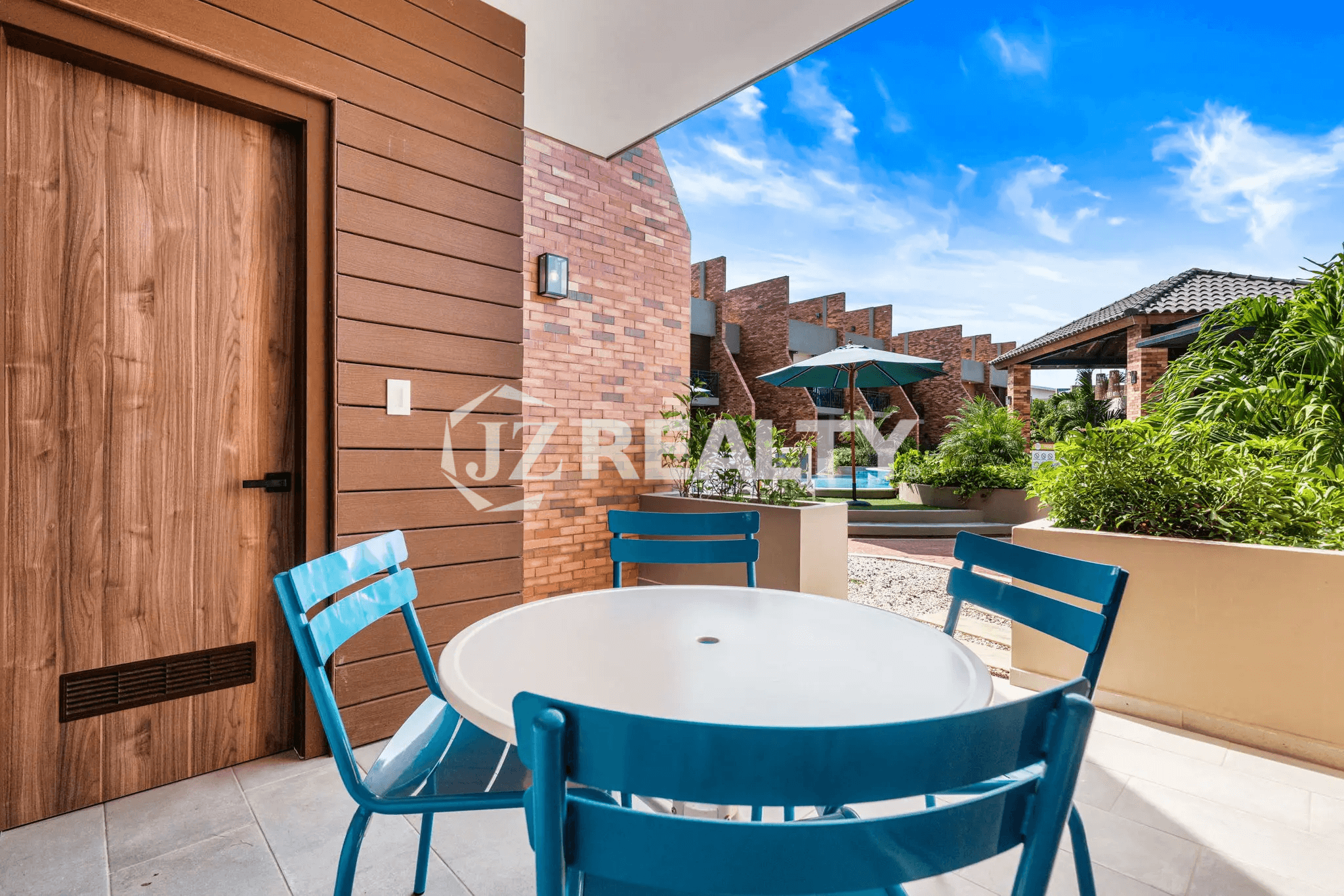 Covered outdoor patio space at Porta al Sole Unit 18 with a small round white table and three blue chairs, showing the view to the resort's exterior and pool area.