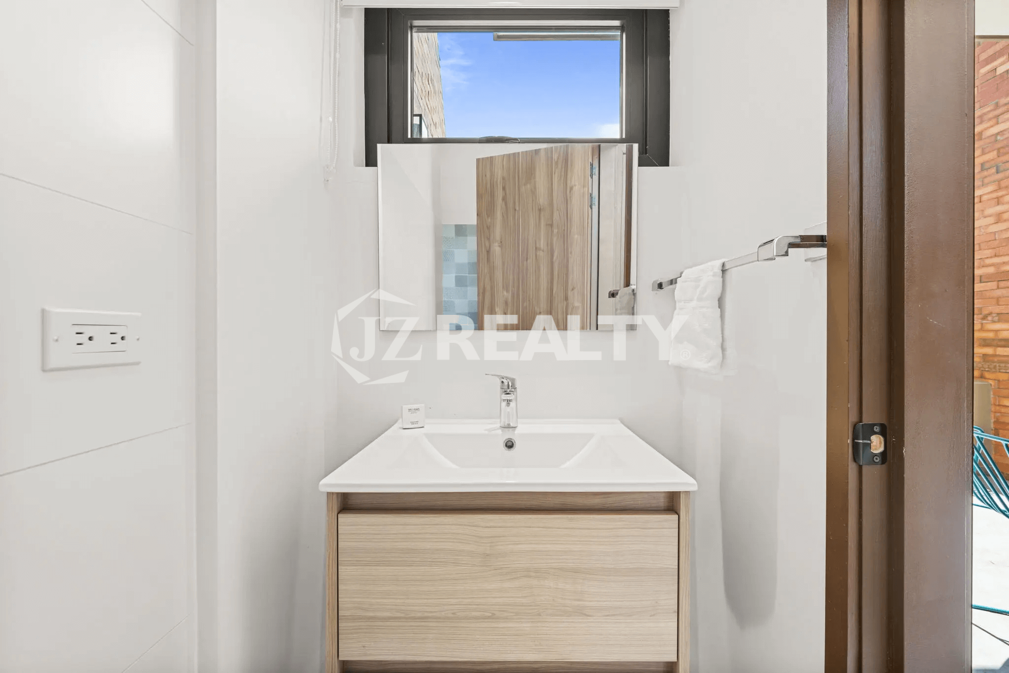 Small ground floor bathroom/half bath vanity in Porta al Sole Unit 18 with a white sink, light wood vanity cabinet, mirror, and white walls with horizontal paneling.