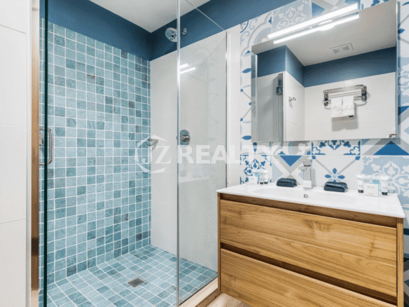 Guest bathroom in Porta al Sole Unit 18 featuring a walk-in shower with blue square mosaic tile, a wood vanity, and white and blue patterned accent wall tile.