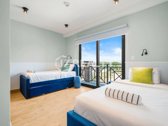 Bright guest bedroom in Porta al Sole Unit 18 featuring two single beds with blue upholstered frames, light wood floor, and a glass door opening to a private balcony.