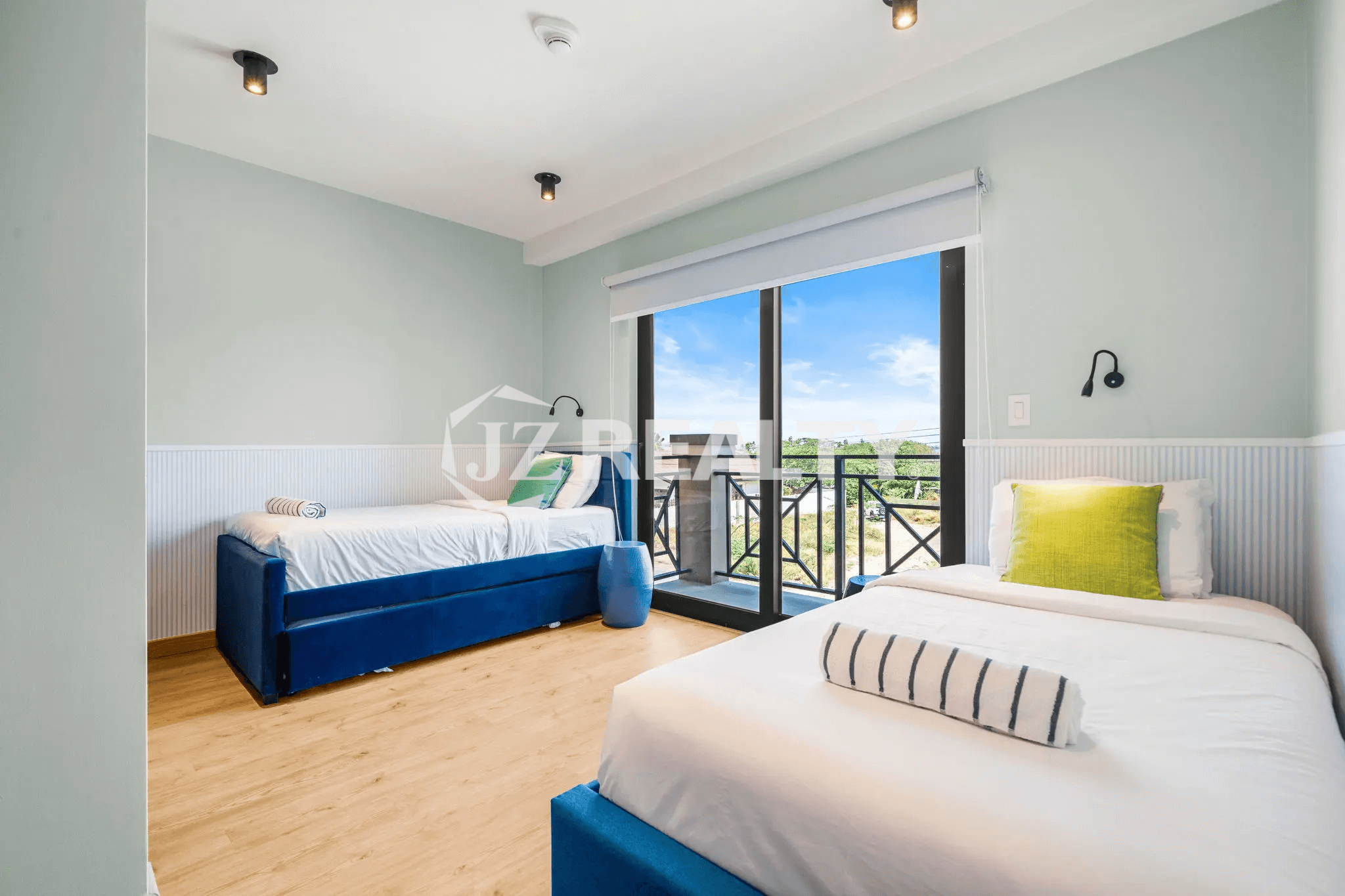 Bright guest bedroom in Porta al Sole Unit 18 featuring two single beds with blue upholstered frames, light wood floor, and a glass door opening to a private balcony.