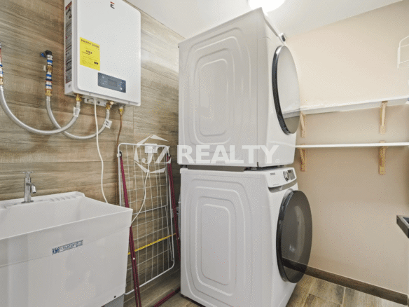 Dedicated laundry room in Porta al Sole Unit 18 with a stacked washer and dryer unit, utility sink, shelving, and a wall-mounted water heater.