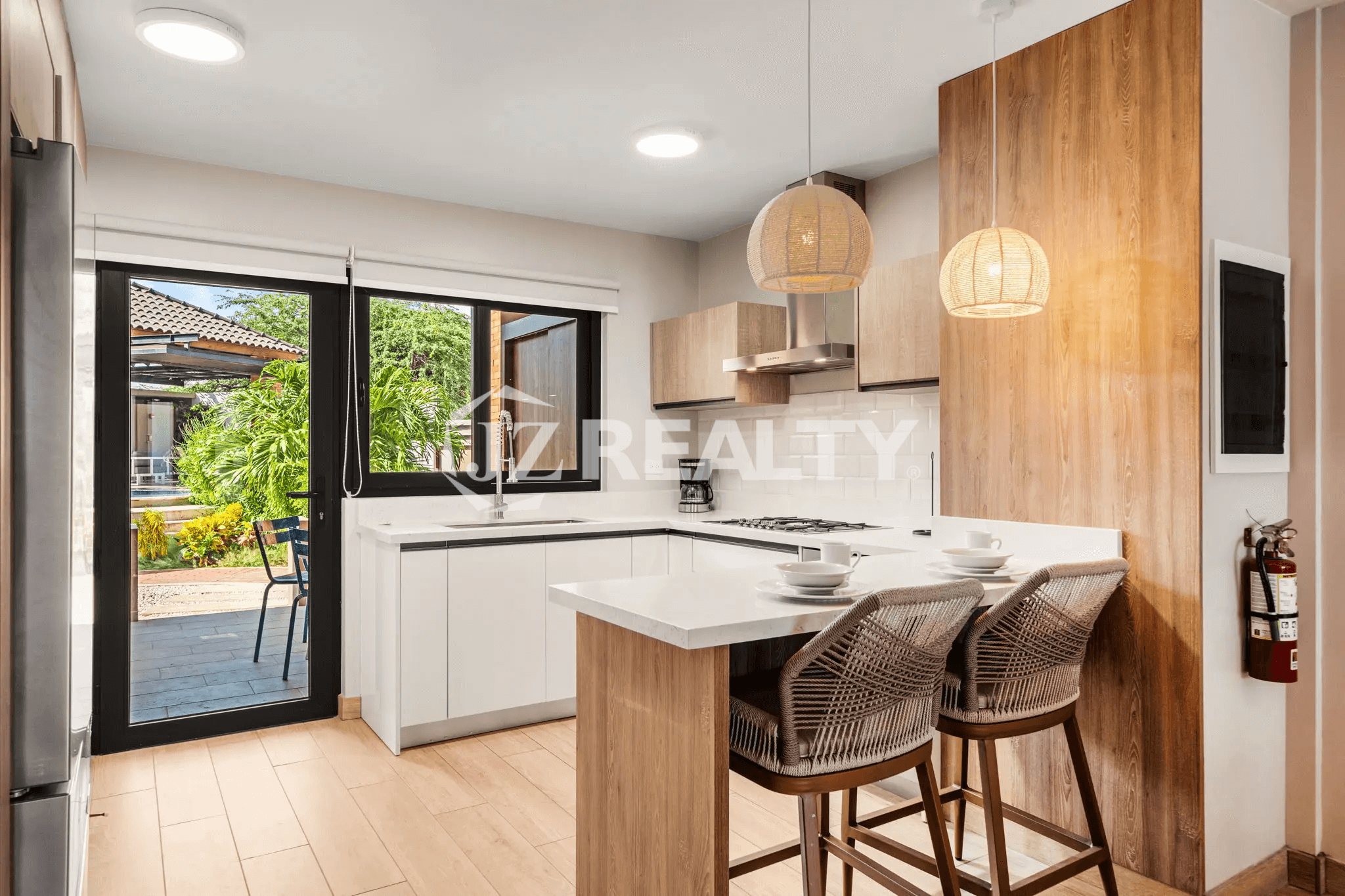 Corner view of the bright kitchen in Porta al Sole Unit 18, showing white subway tile backsplash, gas cooktop, breakfast bar with barstools, and a glass door leading to the outdoor space.