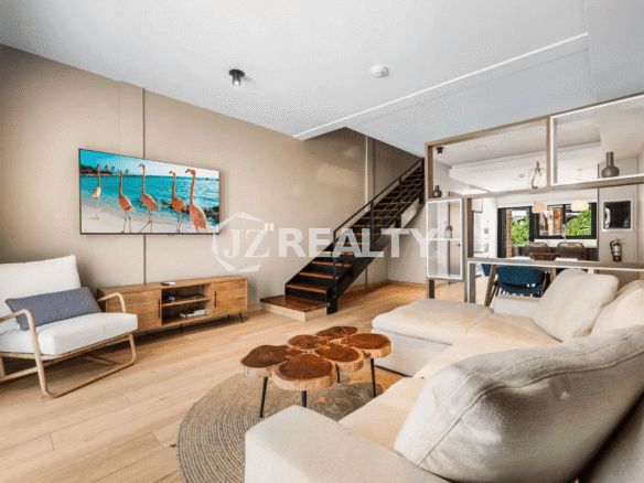 Contemporary living room in Porta al Sole Unit 18 with a wall-mounted TV, media console, comfortable accent chair, and sectional sofa, showing the open concept to the dining and kitchen areas.