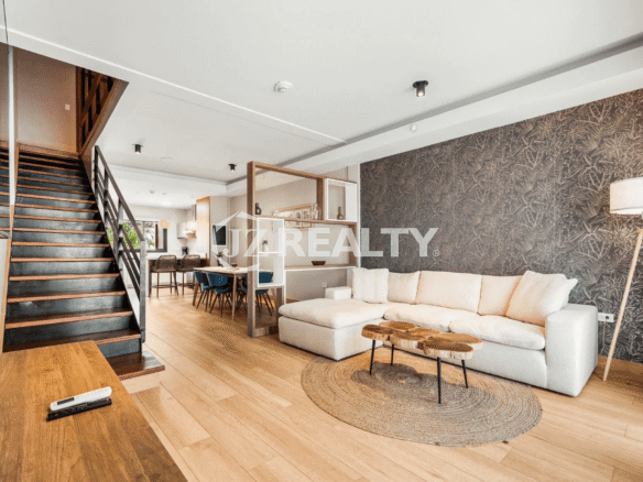 Luxurious living room in Porta al Sole Unit 18 with large sectional sofa, wood coffee tables, textured accent wall, light wood floor, and open staircase leading to upper floors.